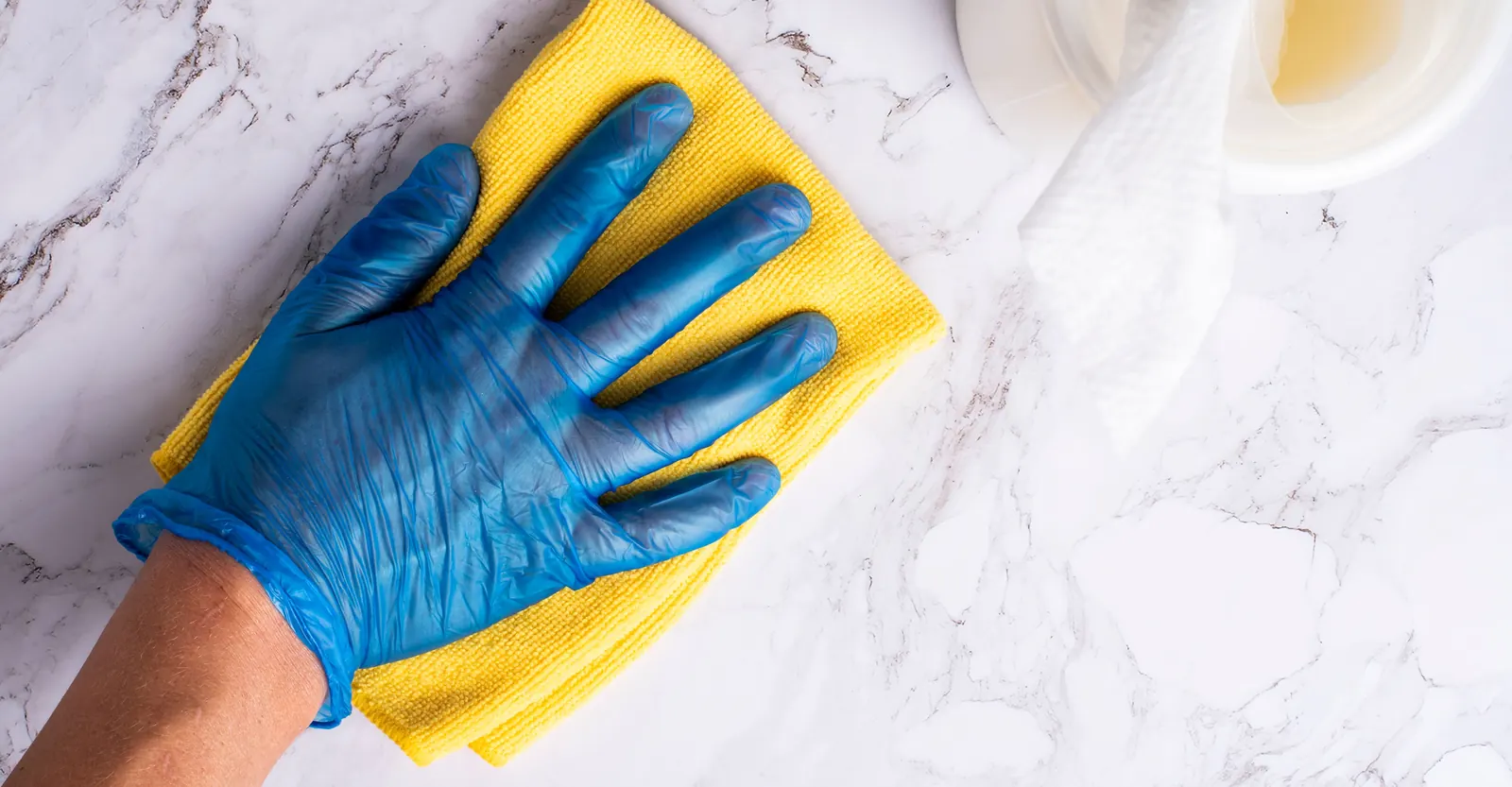 Gloved hand wiping a white marble countertop with a yellow microfiber cloth