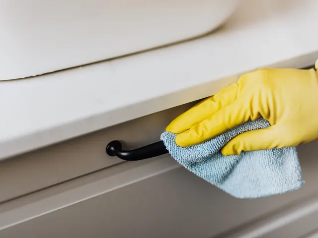 Gloved hand wiping a cabinet drawer front and handle with a microfiber cloth