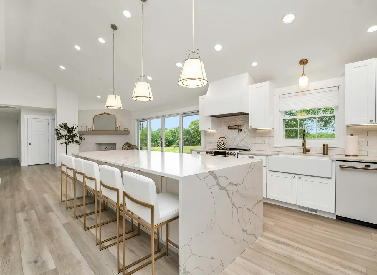 Bright white kitchen with a marble waterfall island, gold-framed bar stools and brass pendant lights