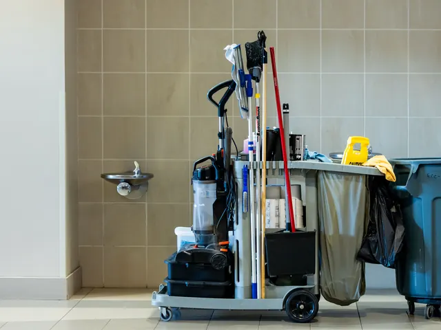 Stocked janitorial cart with mops, vacuum and trash bin in a tiled commercial corridor