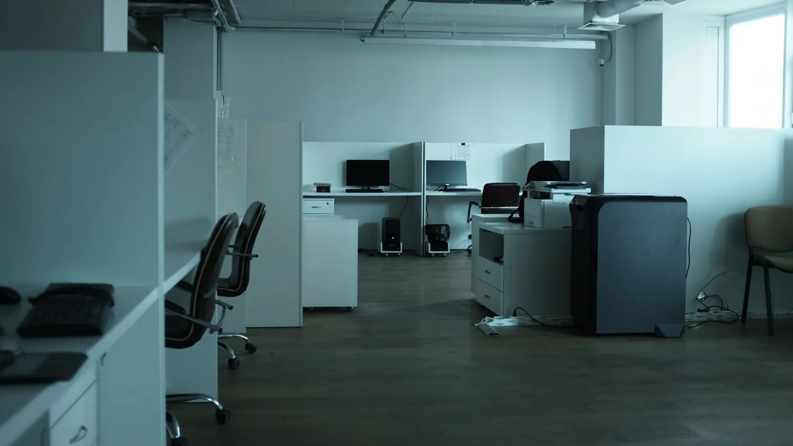 Empty open-plan office with workstations, desk chairs and a printer
