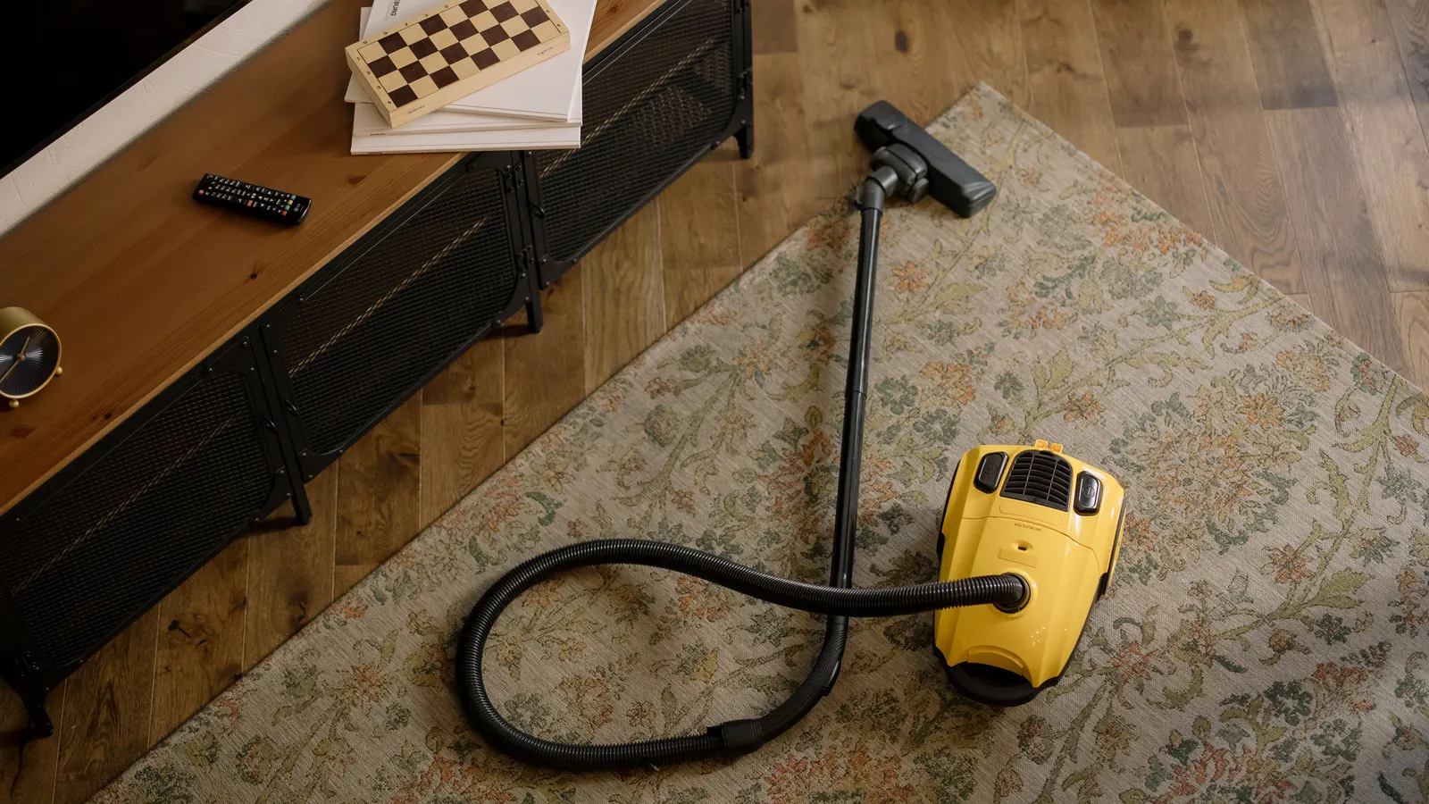 Canister vacuum on a floral area rug beside a wooden TV console in a lived-in living room
