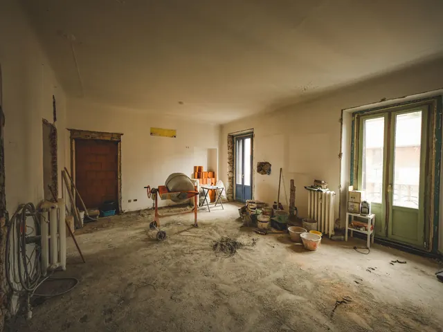 Gutted room under renovation with rubble, a cement mixer and buckets across the floor