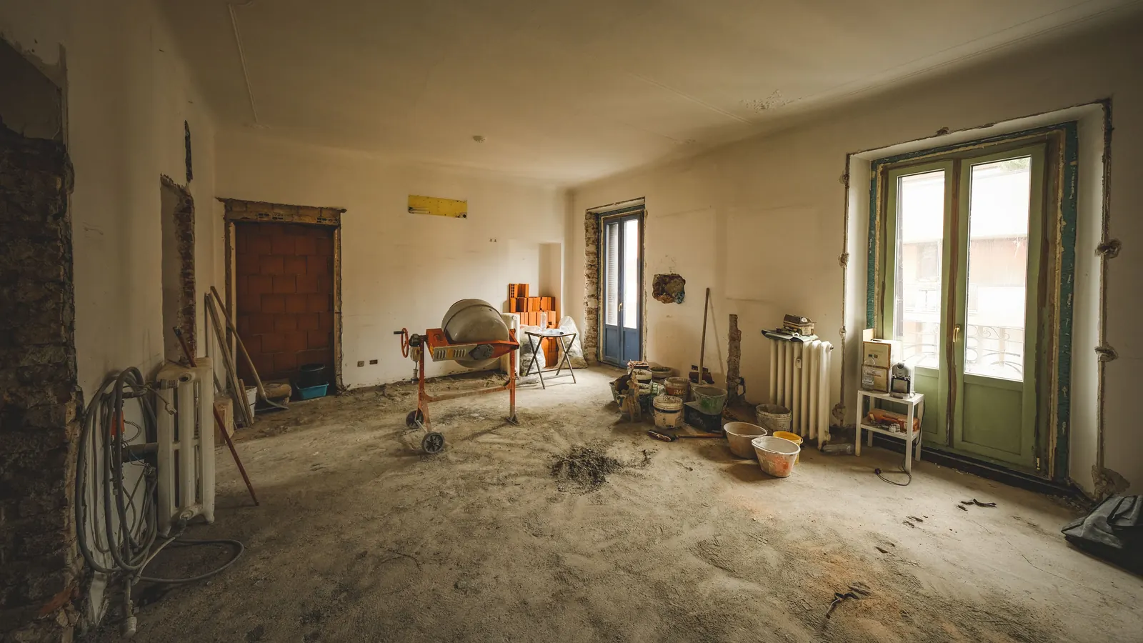 Gutted room under renovation with rubble, a cement mixer and buckets across the floor